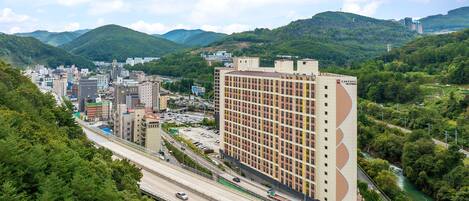 A high-rise hotel with a modern design, located in a mountainous area with a view of a river and surrounding greenery.