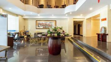 A hotel lobby with a reception desk, seating area, and a staircase leading to an upper level.
