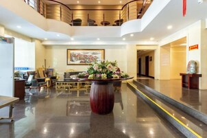 Un hall de hotel con mostrador de recepción, zona de estar y una escalera que conduce a un nivel superior.