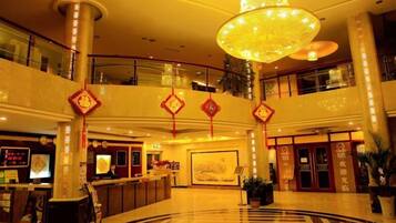 A hotel lobby with a reception desk, a large chandelier, and a circular floor design.
