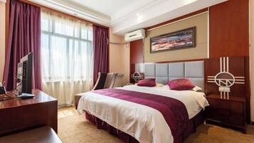 A hotel room with a large bed, a desk, a chair, an air conditioning unit, and a painting on the wall.