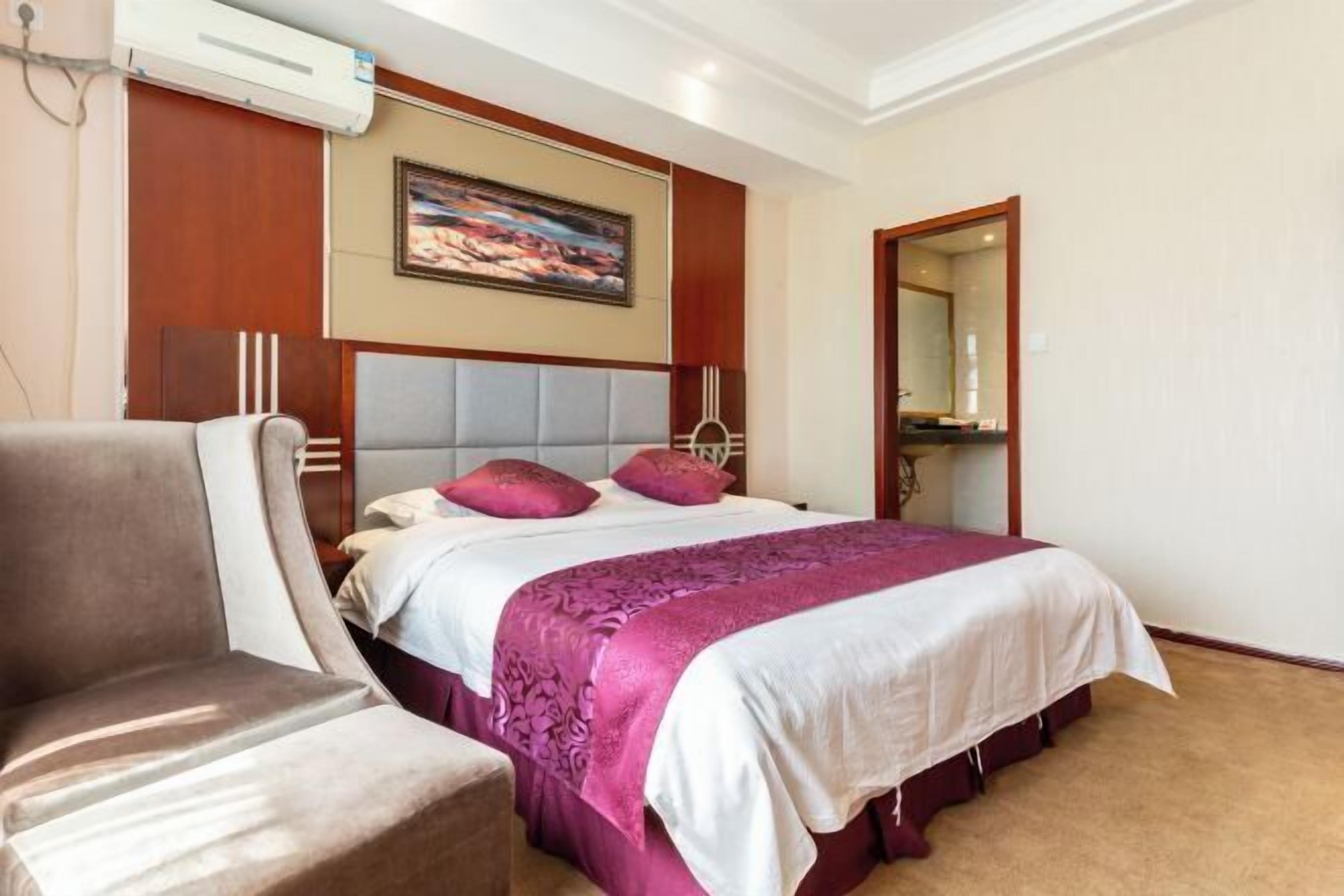 A hotel room with a large bed, a chair, a painting on the wall, and a mirror.