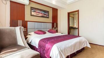A hotel room with a large bed, a chair, a painting on the wall, and a mirror.