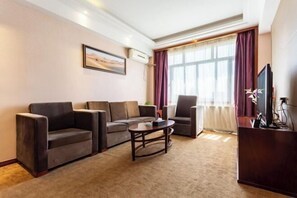 Ein Wohnzimmer mit einer Sofagarnitur, einem Couchtisch, einem Fernseher und einem großen Fenster mit Vorhängen.