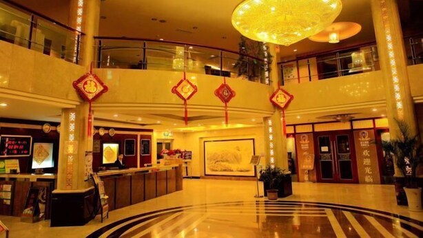 Een hotel lobby met een receptiebalie, een grote kroonluchter en decoratieve rode lantaarns.