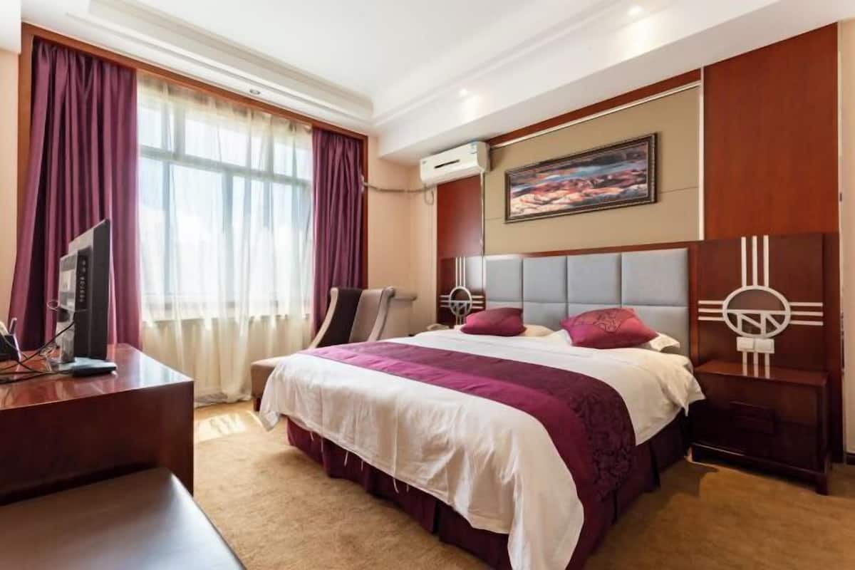 Una habitación de hotel con una cama grande, un escritorio con ordenador, una silla y un televisor.