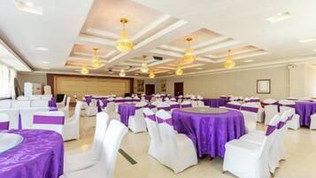 A banquet hall with round tables covered in white tablecloths and purple centerpieces, arranged in rows.