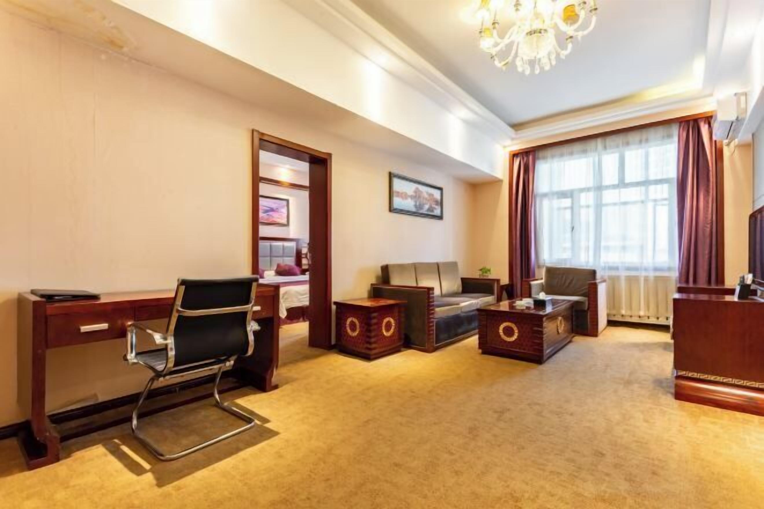 A hotel room with a wooden desk, a black office chair, a sofa, a coffee table, and a TV.