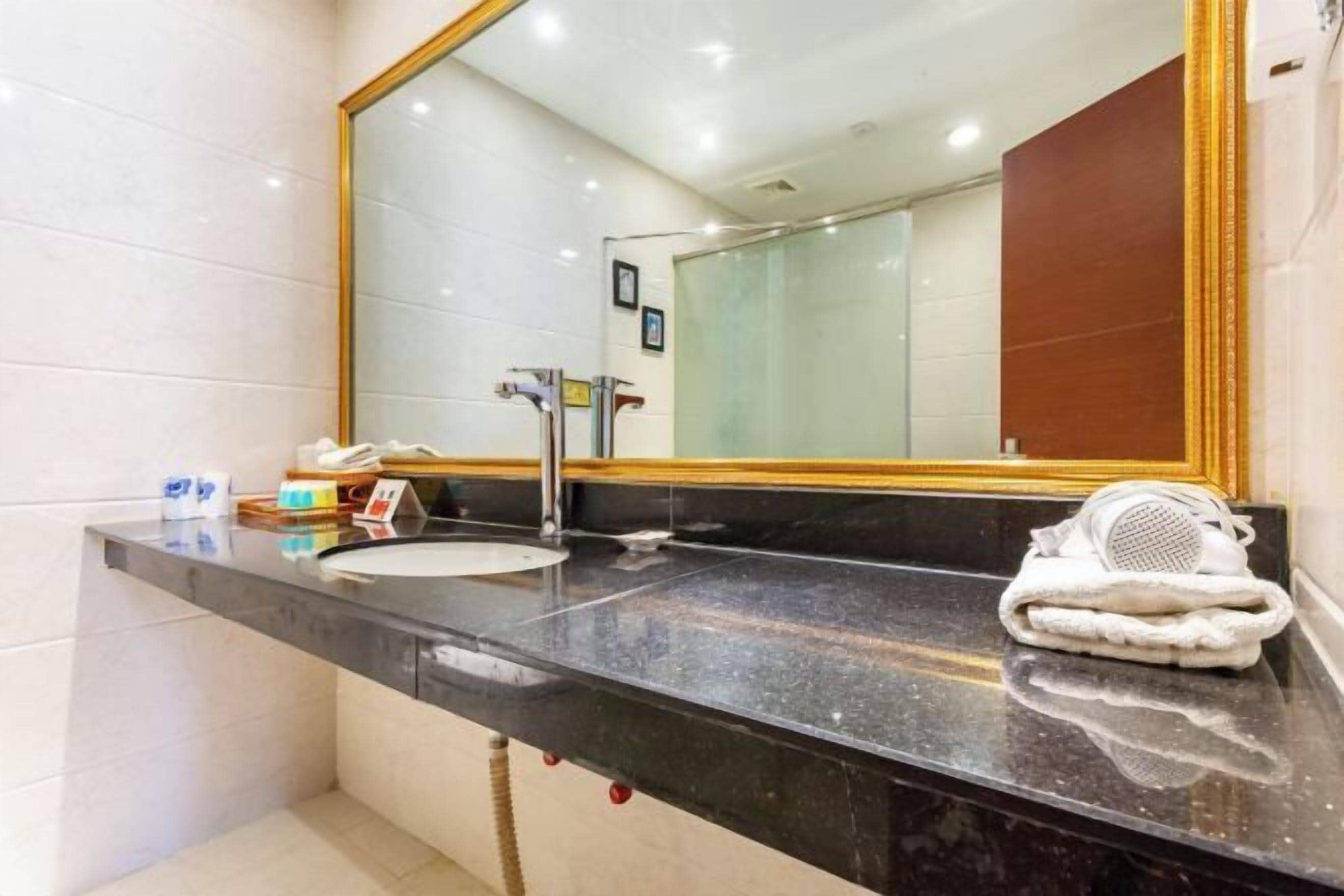 A bathroom with a black countertop, a white sink, a large mirror with a gold frame, and a towel on the counter.