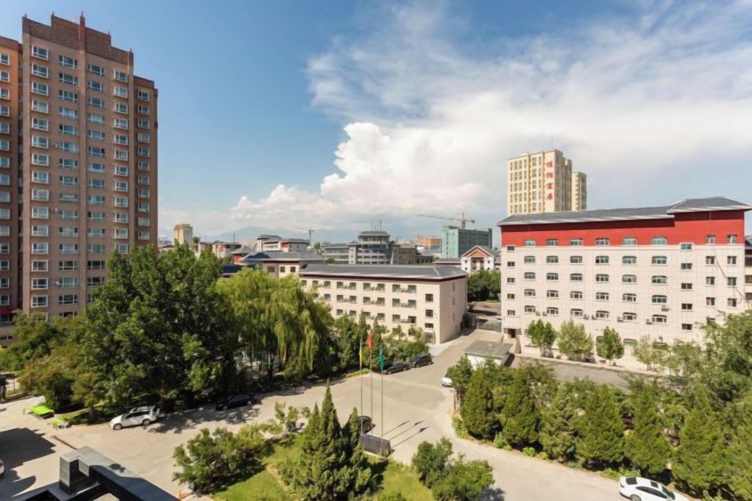 A multi-story building with a parking lot and greenery in the foreground.