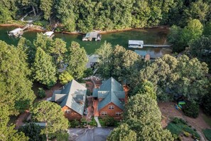 Une grande maison entourée d’une forêt dense et donnant sur un lac où se trouvent des quais.