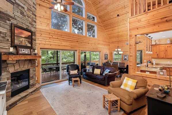 L’intérieur d’une cabane en rondins, avec une cheminée en pierre, un plafond en bois et de grandes fenêtres.