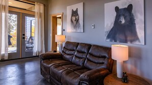A leather sofa, a lamp, and two wall art pieces of a wolf and a bear. - Lakeshore Lodging Inlet View Home (Homer)