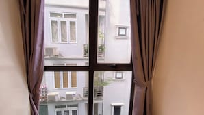 A window with brown curtains, revealing a building with multiple air conditioning units and balconies. - Era Apartment Ha Yen Quyet (Hanoi)
