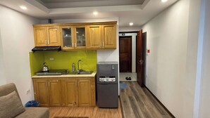 A compact kitchen with wooden cabinets, a sink, a kettle, and a refrigerator. - Era Apartment Ha Yen Quyet (Hanoi)