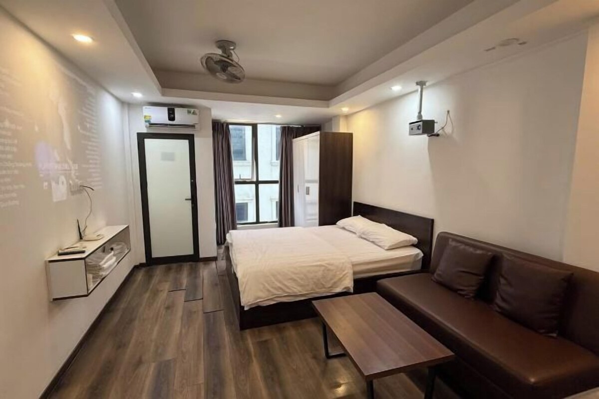 A modern hotel room with a bed, a sofa, a small table, and a ceiling fan.
