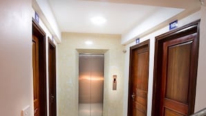 A hallway with a central elevator, wooden doors, and a metal handrail. - Era Apartment Ha Yen Quyet (Hanoi)