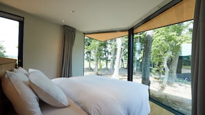 A bedroom with a large bed, a window with a view of trees, and a wooden headboard. - SONEKA (Kitahiroshima)