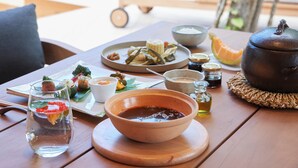 A dining table with various dishes and a teapot, surrounded by lounge chairs and a view of a modern building and trees. - SONEKA (Kitahiroshima)