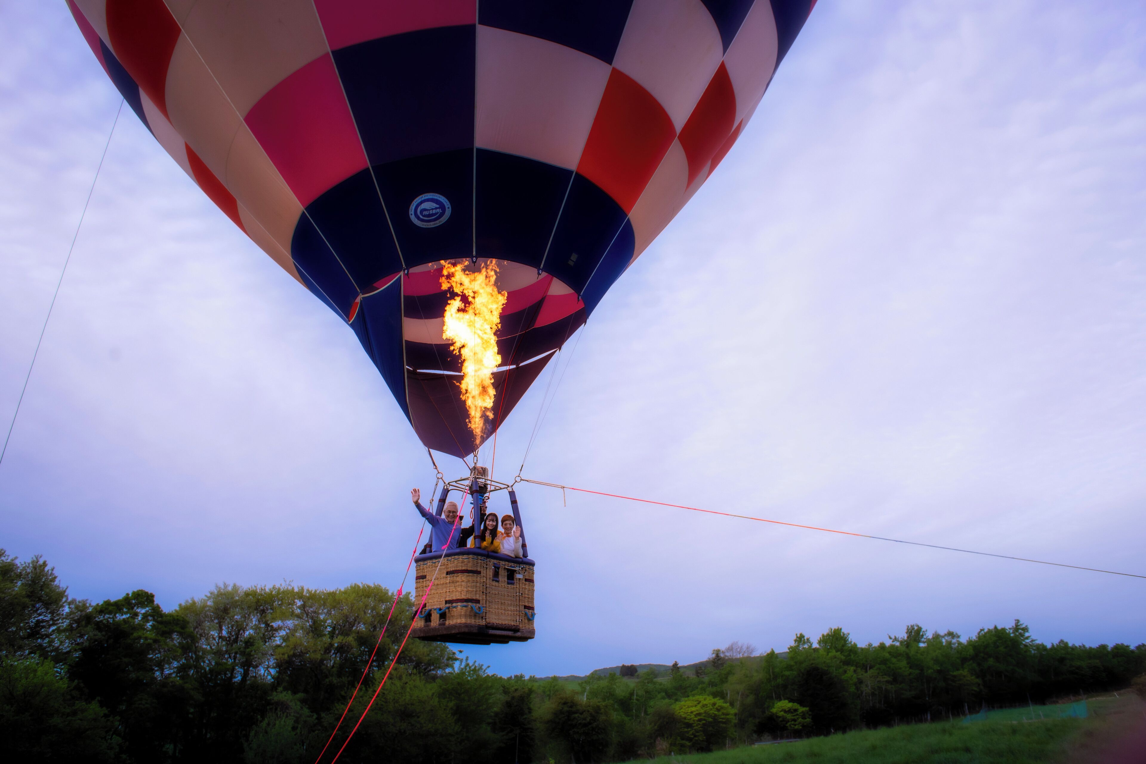 A hot air balloon with passengers, flames at the basket, and a clear sky.