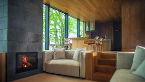 A modern living room with a fireplace, a sofa, and a dining area with wooden furniture. - SONEKA (Kitahiroshima)