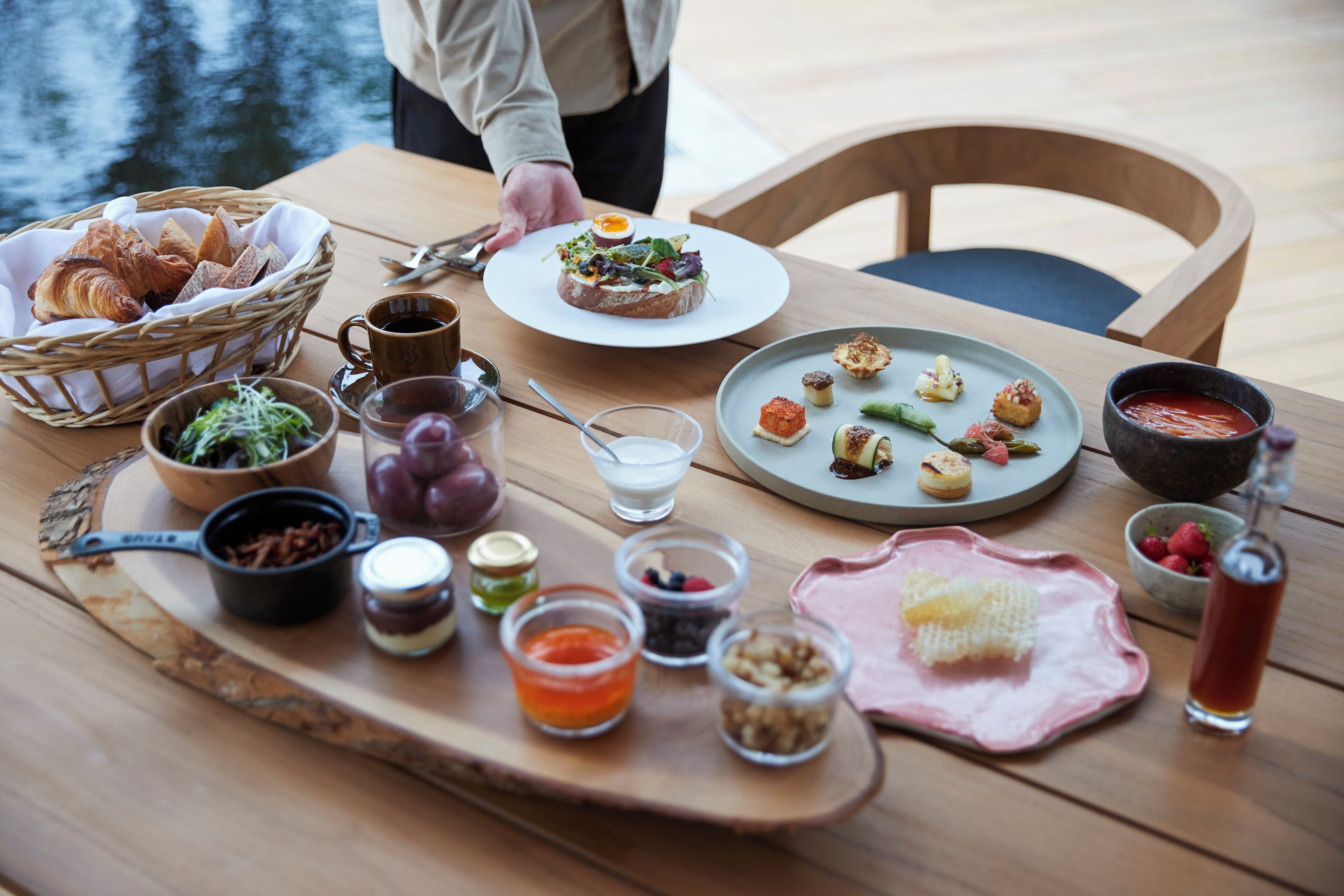 A table set with various food items and condiments, including croissants, a plate of appetizers, and a drink.