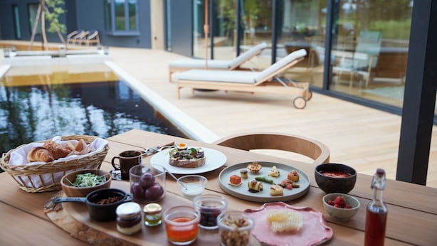 A dining table with food and drinks, a pool, and lounge chairs in a modern setting. - SONEKA (Kitahiroshima)