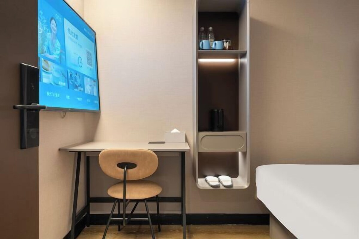 Ett hotellrum med en säng, ett skrivbord med en stol, en hylla med toalettartiklar och en tv-skärm som visar innehåll.