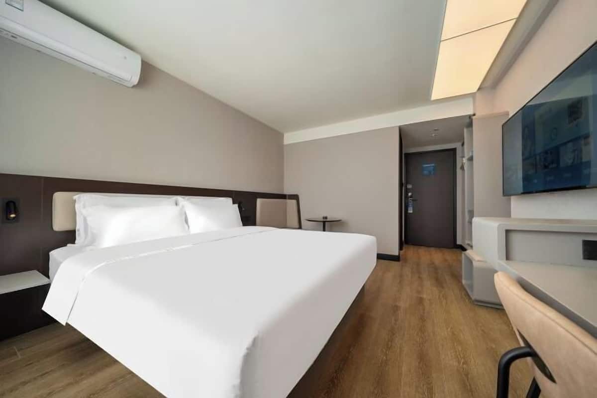 Une chambre d’hôtel avec un lit, une table de chevet, une lampe et un téléviseur fixé au mur.
