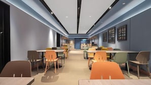 A modern dining area with multiple tables and chairs, a kitchen in the background, and a blue accent wall. - HanTing Hotel (Xiamen Wenzao The MixC) (Xiamen)