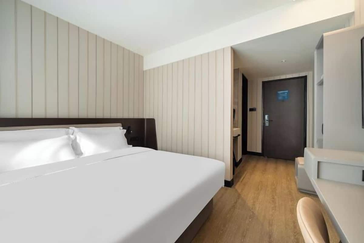 Une chambre d’hôtel avec un grand lit, un bureau et une porte donnant sur un couloir.