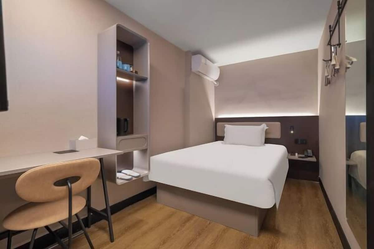 Une chambre d’hôtel de taille réduite, comprenant un lit, un bureau, une chaise, une armoire et une table de chevet.