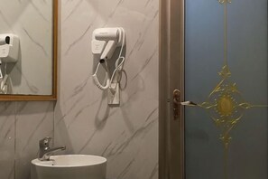 Een badkamer met een marmeren wand, een wastafel, een haardroger en een deur met een decoratieve gouden knop.