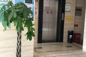 Un ascensor con un letrero que indica el cuarto piso, un contenedor de basura y una caja roja con texto en la pared.