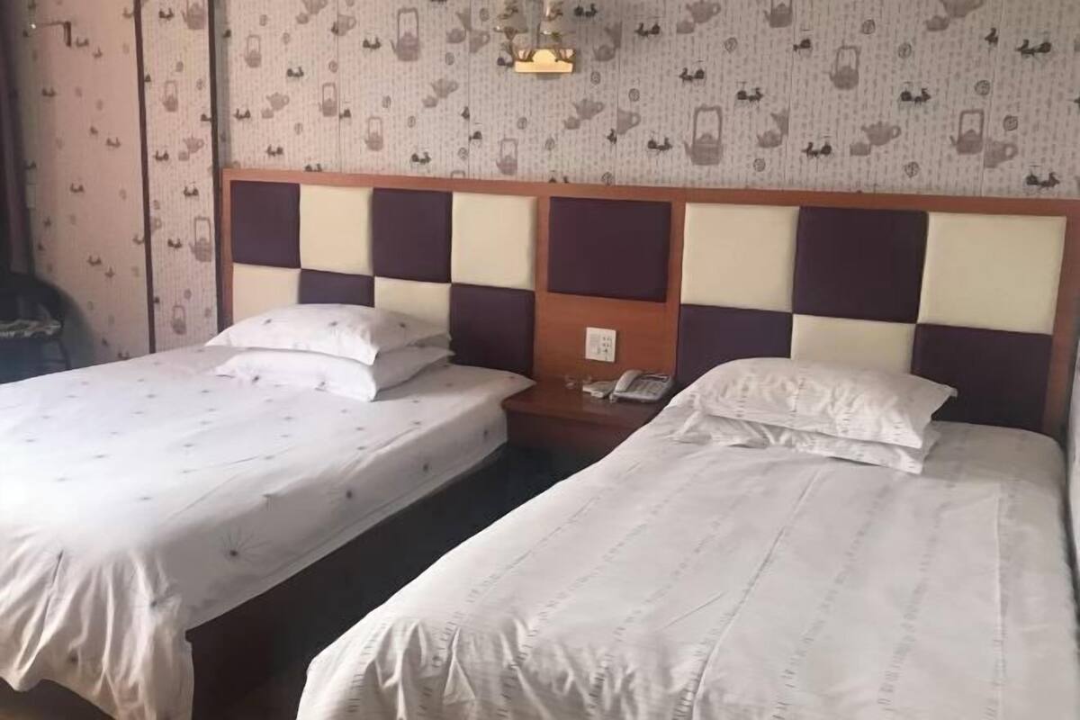 A hotel room with two beds, a wooden headboard, a telephone, and patterned wallpaper.