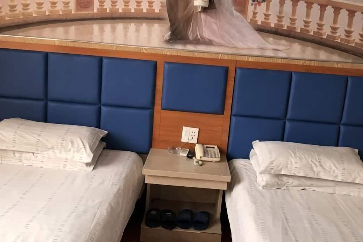 A hotel room with two beds, a nightstand with a phone, and a shoe rack.