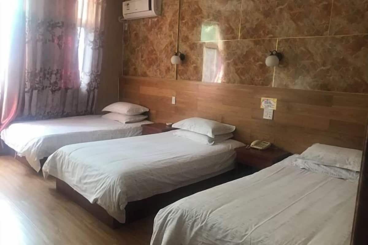 A hotel room with three beds, a wooden headboard, a wall-mounted phone, and a window with curtains.