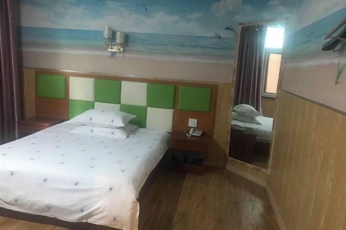 A hotel room with a bed, a nightstand, a mirror, and a wall mural.