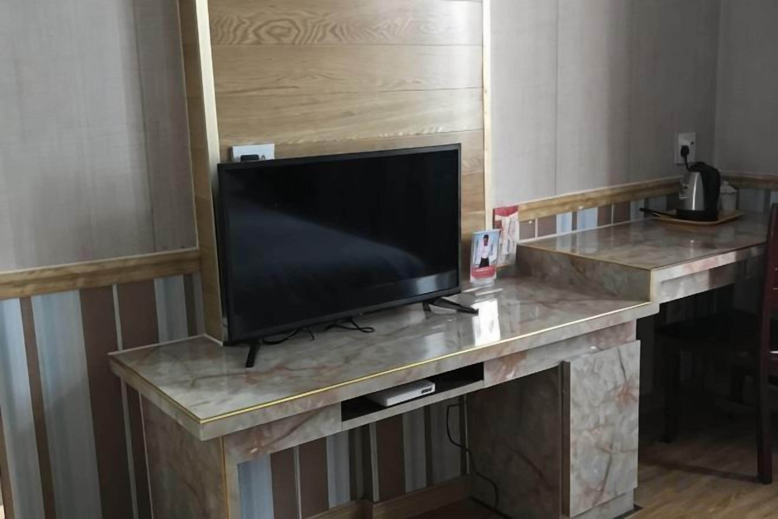 A television on a marble countertop, a coffee maker, and a small cabinet below the TV.