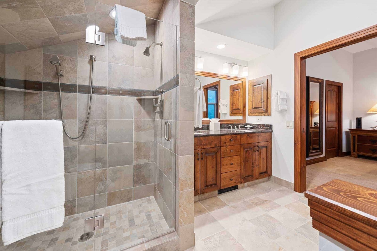 A modern bathroom with a glass-enclosed shower, wooden cabinets, and a large mirror.