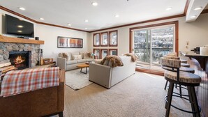 A cozy living room with a fireplace, a sofa, a coffee table, and a bar area with stools. - 2 Bedroom Residence in the Heart of Beaver Creek Village - Ski In, Ski Out (Avon)