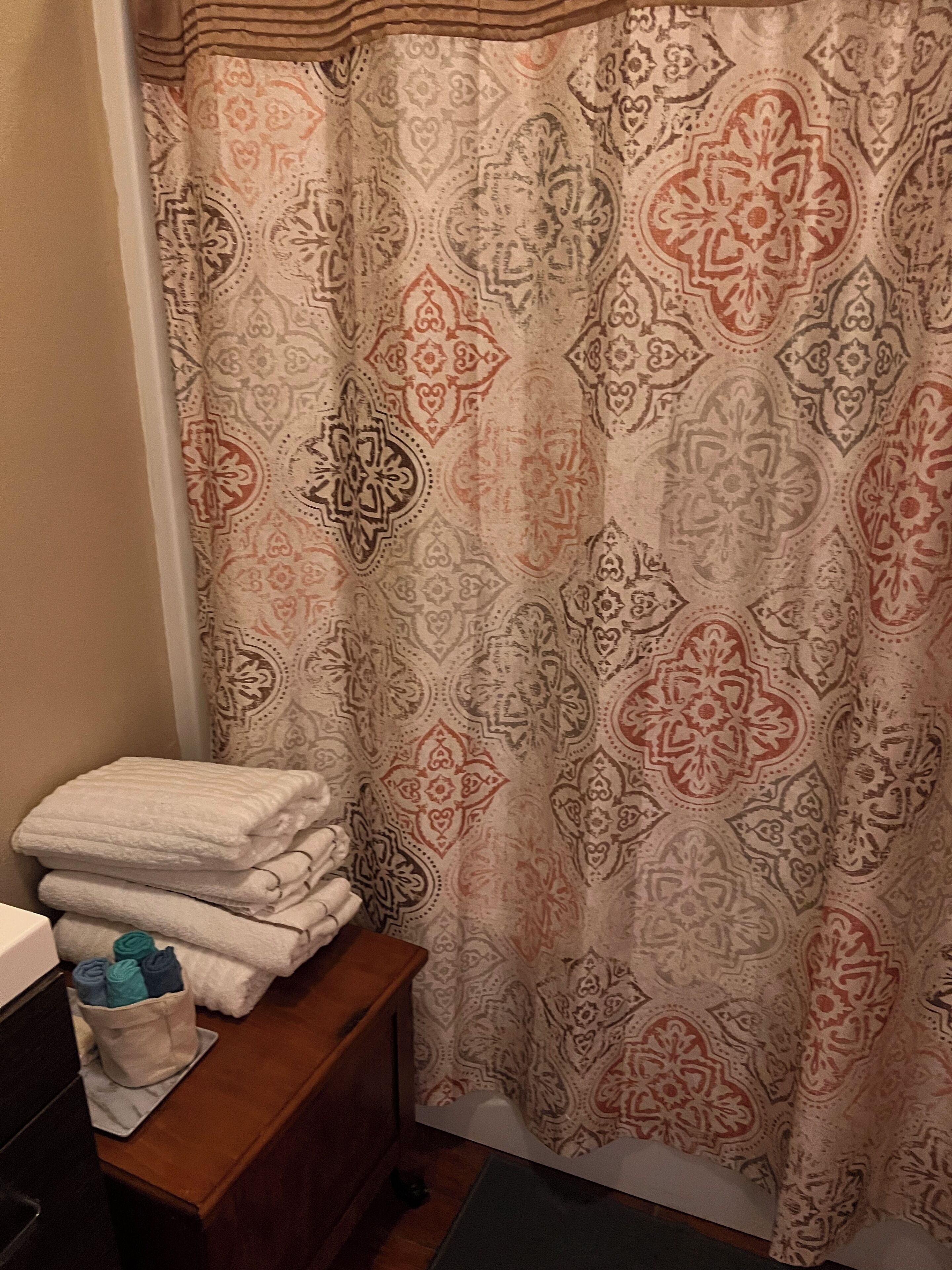 Un baño con cortina de ducha estampada, una pila de toallas dobladas y un taburete de madera pequeño.