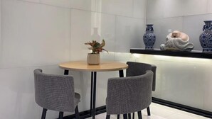 A modern dining area with a round table and two grey chairs, a potted plant, and decorative vases on a shelf. - Jinglai Hotel·Selection (Shanghai Hong Qiao Weining Road Subway Station) (Shanghai)
