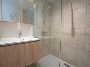 Un baño moderno con cabina de ducha de vidrio, un lavabo blanco y muebles de madera.