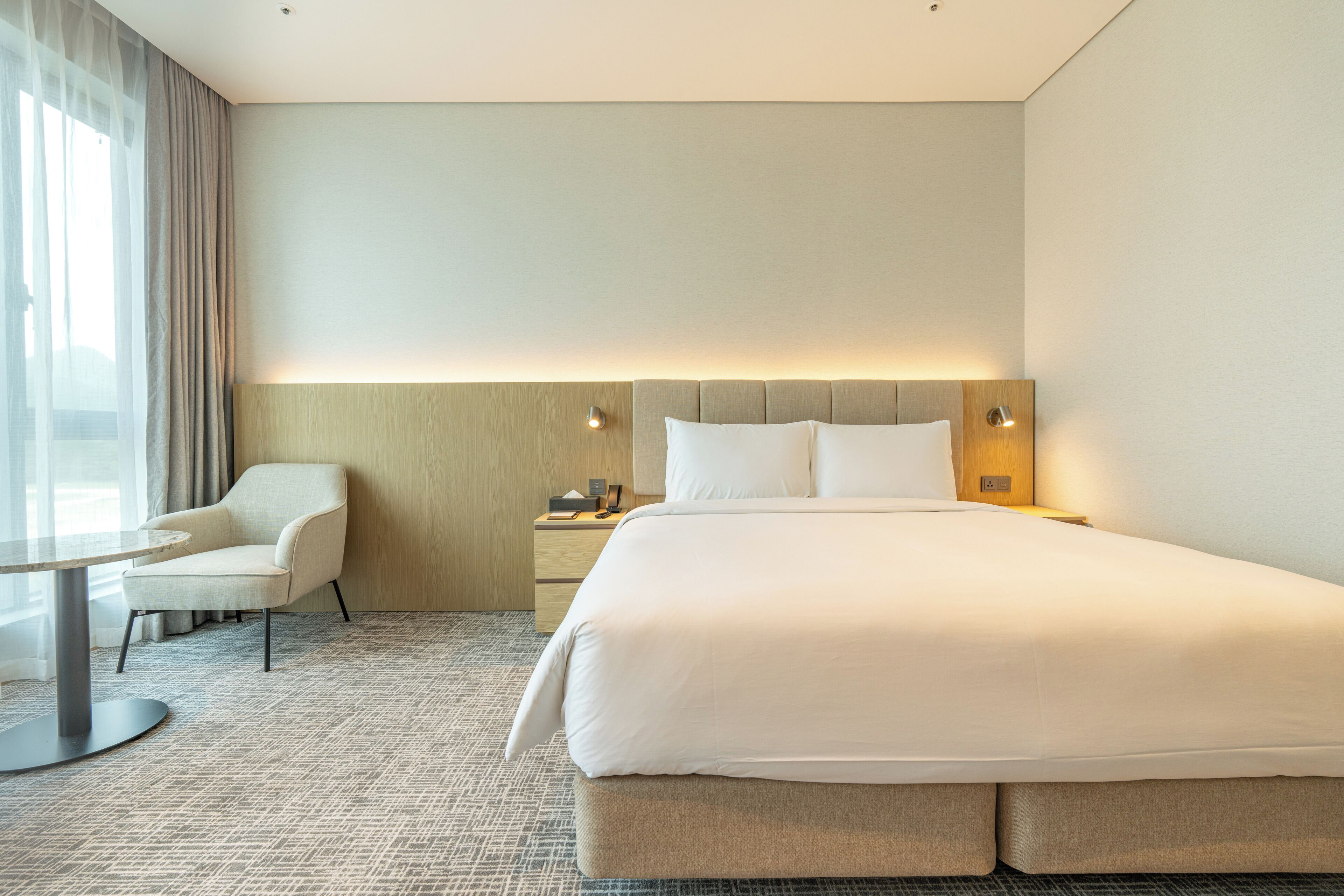 Une chambre d’hôtel avec un grand lit, une chaise, une table de chevet et une lampe.