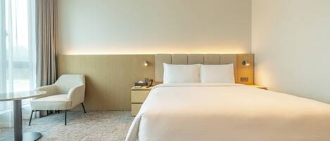Une chambre d’hôtel avec un grand lit, une chaise, une table de chevet et une lampe.