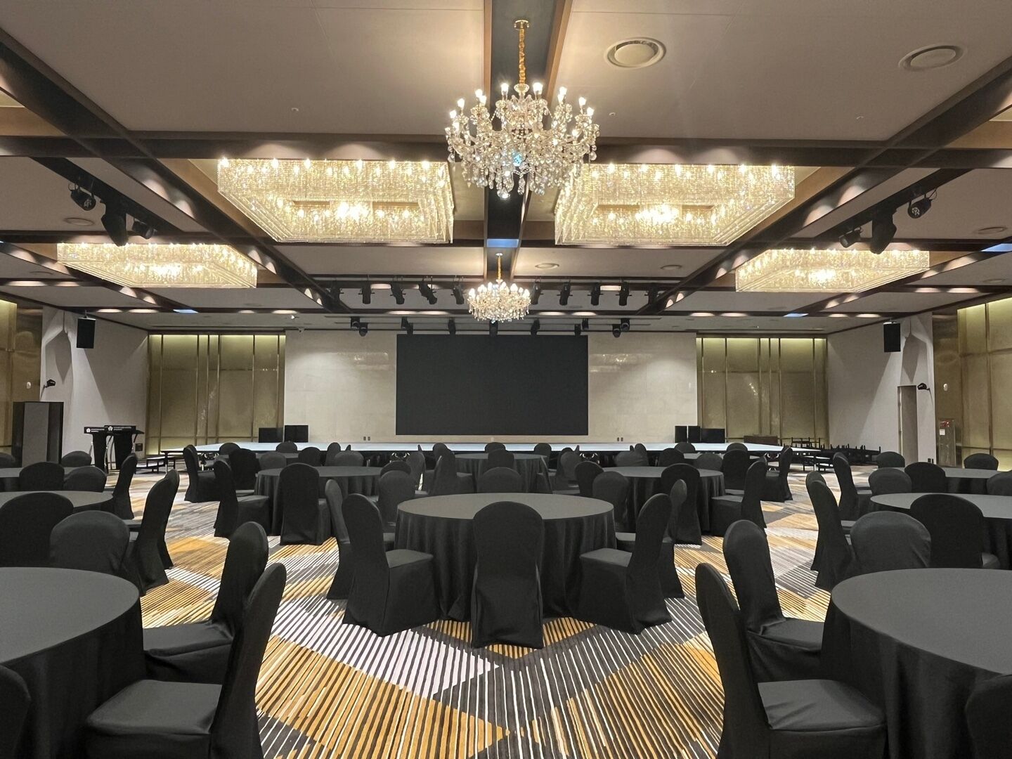 A conference room with a large screen, multiple tables, and chairs.