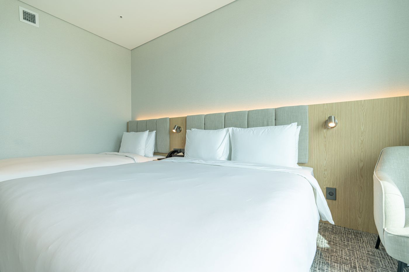 Habitación de hotel con una cama grande, una mesita de noche, una silla y una lámpara fijada a la pared.