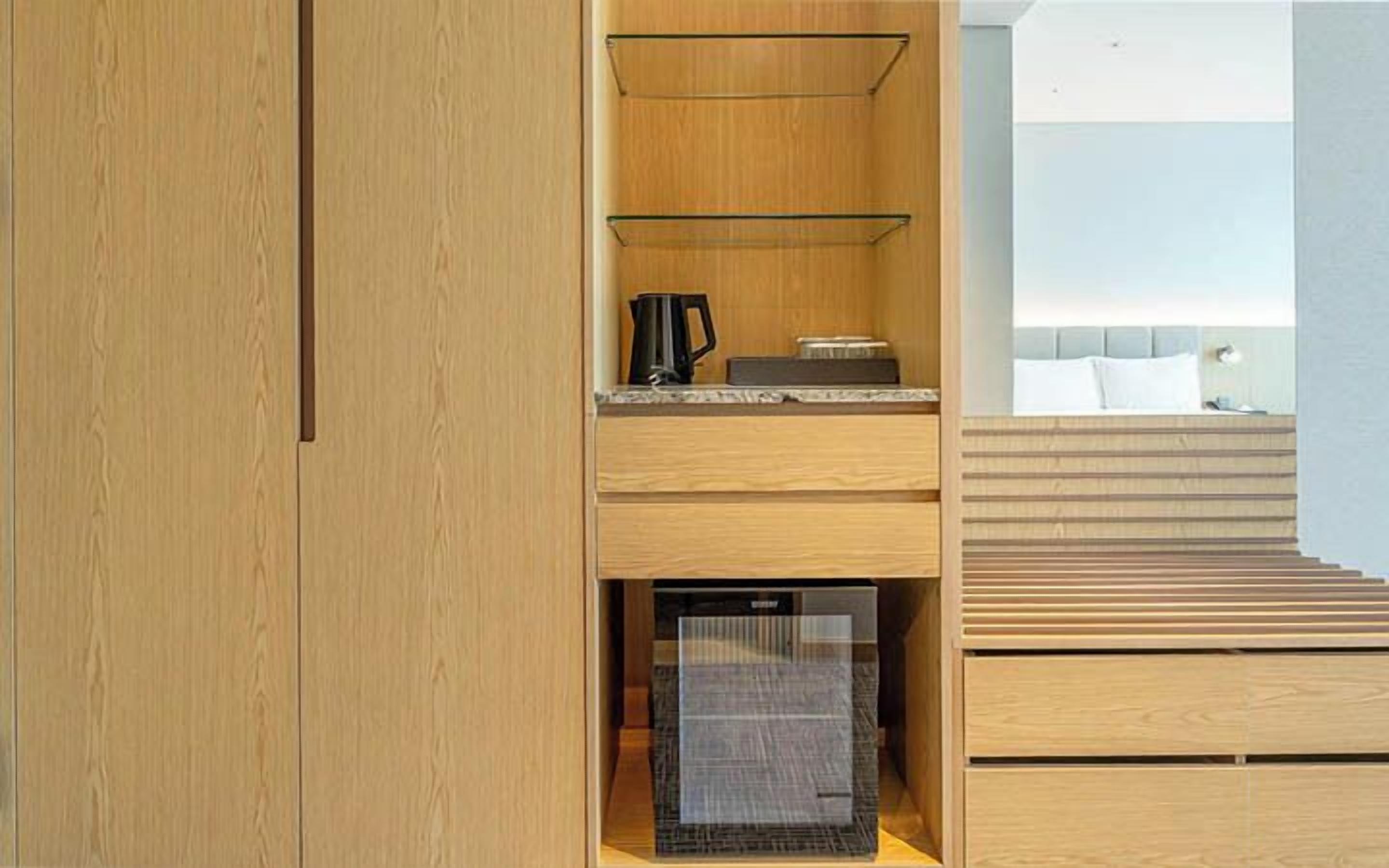 A compact room with a wooden wardrobe, a small kitchenette with a coffee maker, and a built-in mini-fridge.