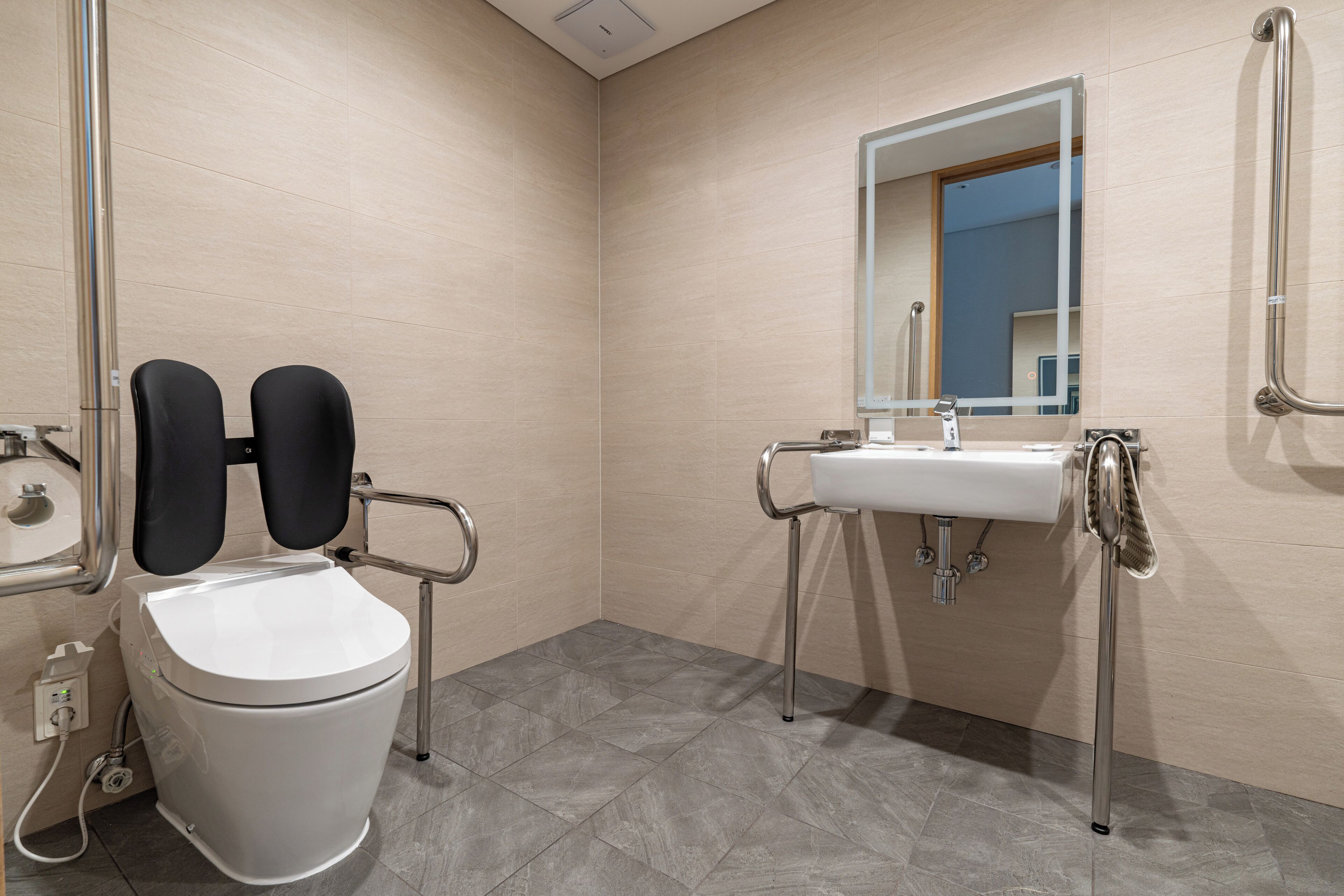 A modern bathroom with a white toilet, a sink with a mirror, and a handrail.